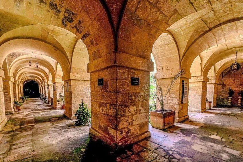 An ancient stone corridor with arches, columns, and potted plants. 2