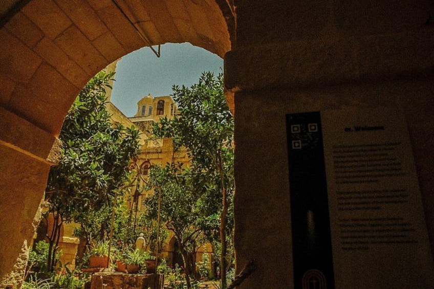 An archway leading to a building with a bell tower, surrounded by greenery. 3