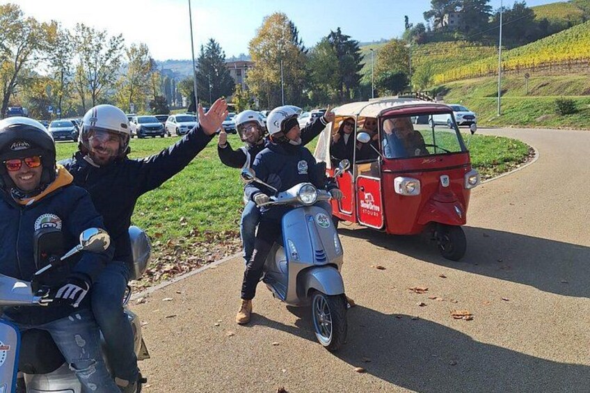 A group of people on scooters and a red three-wheeled vehicle on a road with greenery and buildings in the background. 5