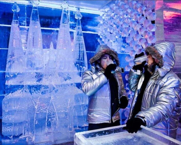 Two people in metallic jackets performing in front of an ice sculpture. 1