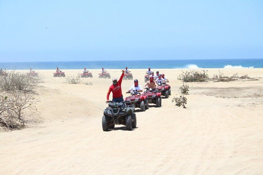 Een groep mensen op terreinwagens op een zanderig strand, met de oceaan op de achtergrond. 4
