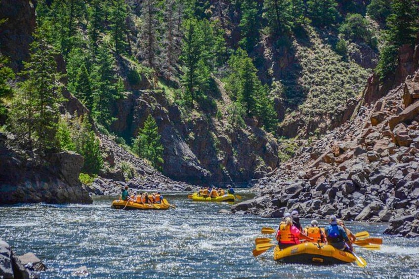 People rafting on a river surrounded by rocky cliffs and dense forest. 1