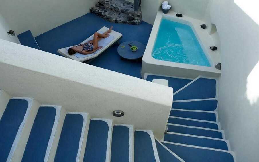 A person sunbathing on a lounge chair by a pool, a hot tub, and a staircase. 2