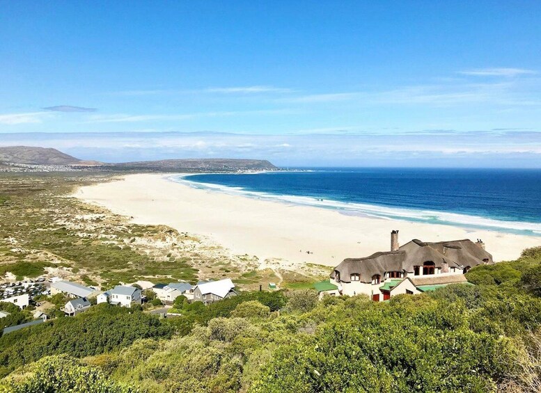 A coastal landscape with a sandy beach, a few houses, and a large body of water. 3