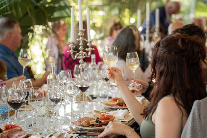 People dining at an outdoor event with wine glasses and plates of food. 4