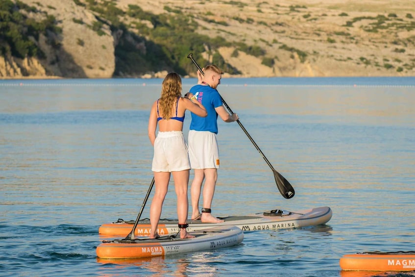 Two people paddleboarding on a calm body of water with a rocky coastline in the background. 3