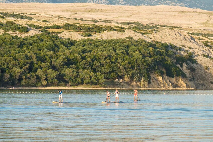 People paddleboarding on a calm lake with a hilly landscape in the background. 2