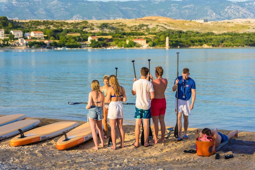 A group of people preparing for paddleboarding on a lake with mountains in the background. 4