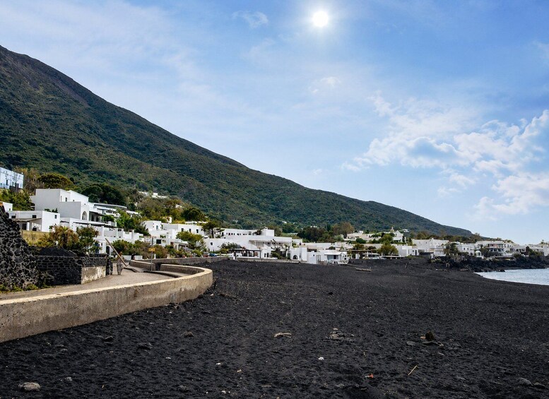 A coastal village with white buildings, a black sandy beach, and a green mountain in the background. 5