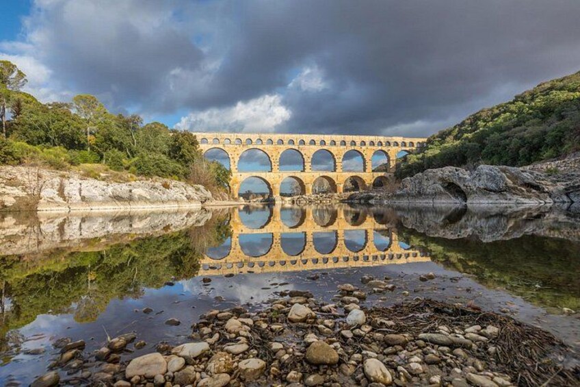 Eine Steinsche Brücke mit Bögen über einem ruhigen Fluss, umgeben von Grün und Felsen. 5