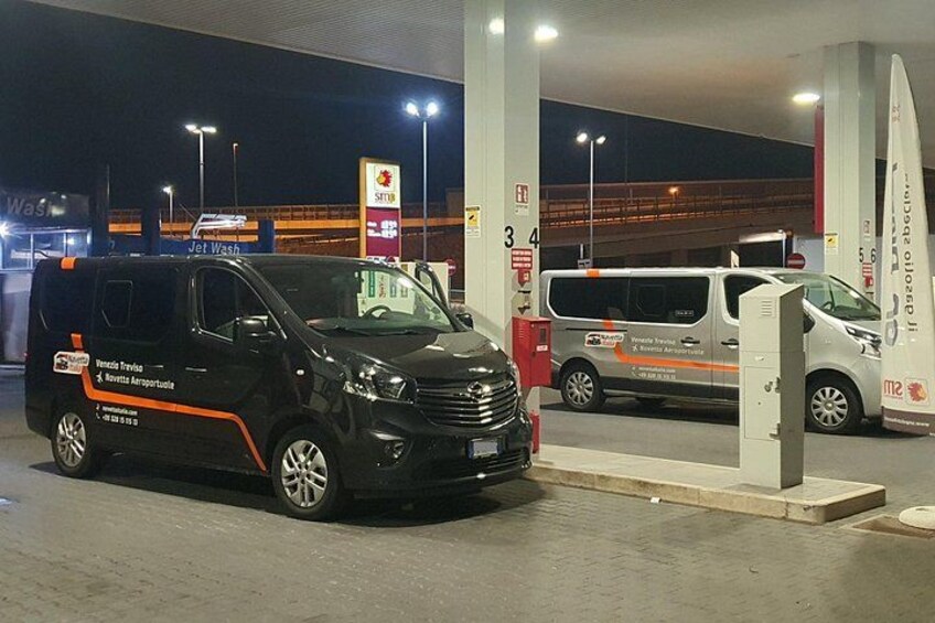 Eine Tankstelle bei Nacht mit zwei geparkten Transportern, einem schwarzen und einem weißen, und einer Zapfsäule im Vordergrund. 4