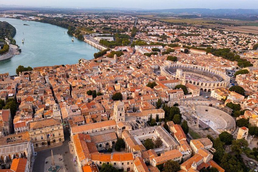 Ein Luftbild einer historischen Stadt mit einem markanten Amphitheater, einem Fluss und dichter Bebauung. 2