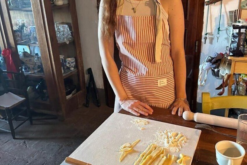 A person in a striped apron working with pasta on a cutting board in a kitchen. 4
