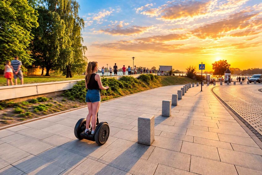 A person riding a Segway on a paved path, with a sunset in the background and a crowd of people in the distance. 5