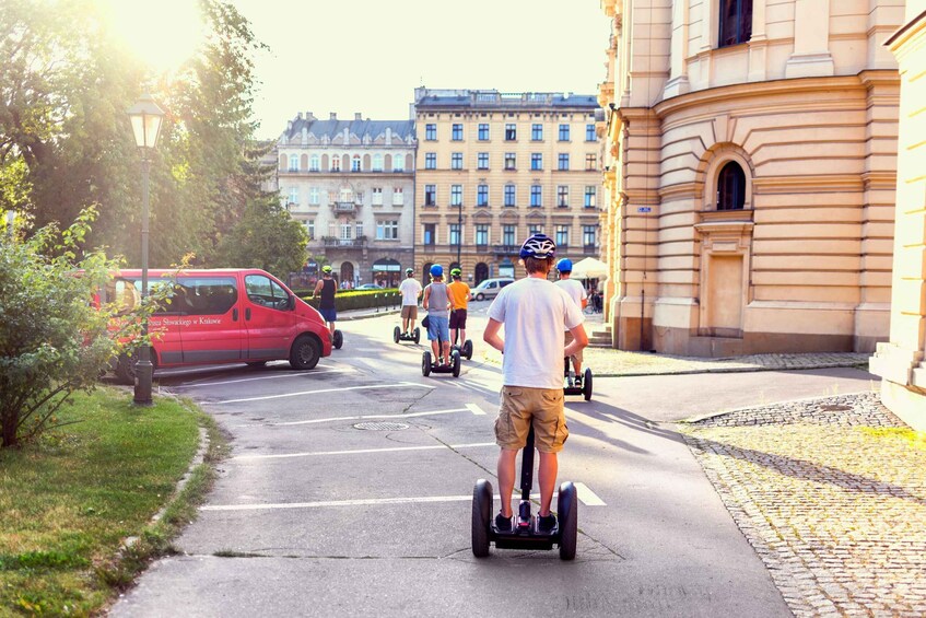 People riding segways on a city street with buildings and a red car in the background. 2