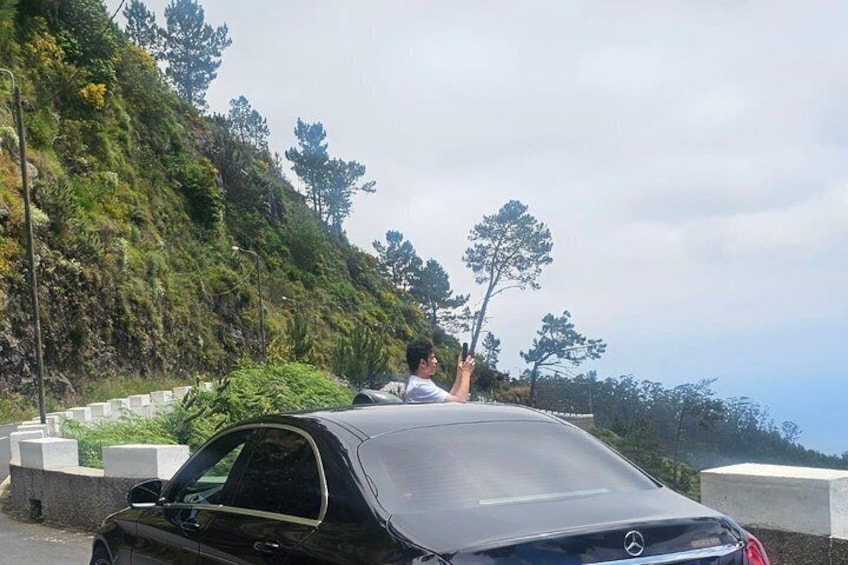 A black car parked on a road with a hilly landscape in the background. 5