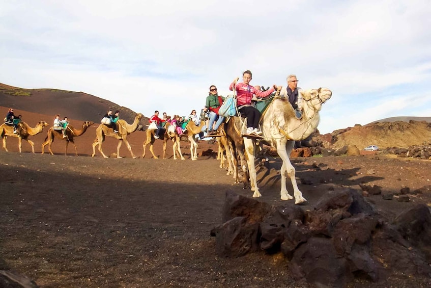 A group of people riding camels on a rocky terrain with hills in the background. 2