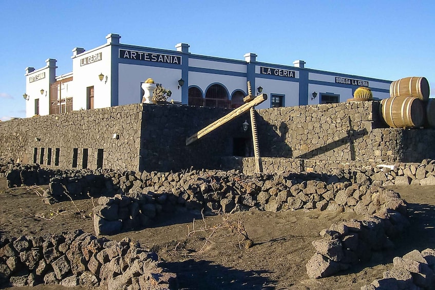 A building with 'ARTESANIA' and 'LA GERIA' signs, stone walls, and barrels. 5