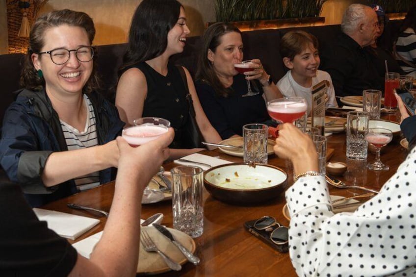 Un grupo de personas sentadas en una mesa en un restaurante, sosteniendo bebidas. 1