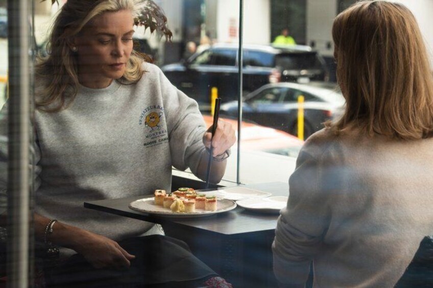 Dos personas sentadas a una mesa con comida, un coche estacionado afuera y un edificio al fondo. 4