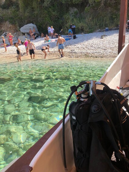 A boat with scuba diving equipment, clear shallow water, and people on a pebbly beach. 2
