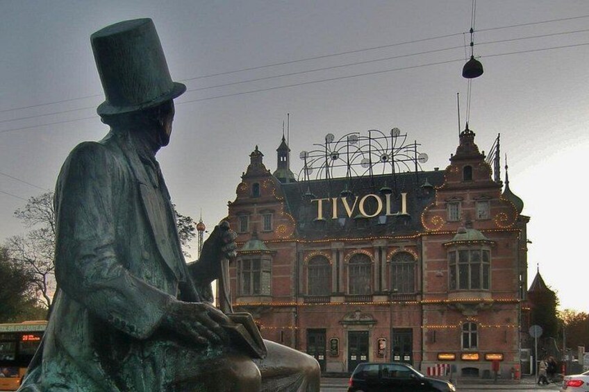 Eine Statue eines Mannes mit Zylinder, ein Gebäude mit der Aufschrift 'TIVOLI' und ein Riesenrad im Hintergrund. 3