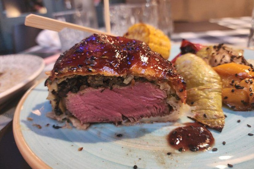 Een bord met een plakje vleesgerecht, mogelijk rosbief, vergezeld van geroosterde groenten en saus. 5