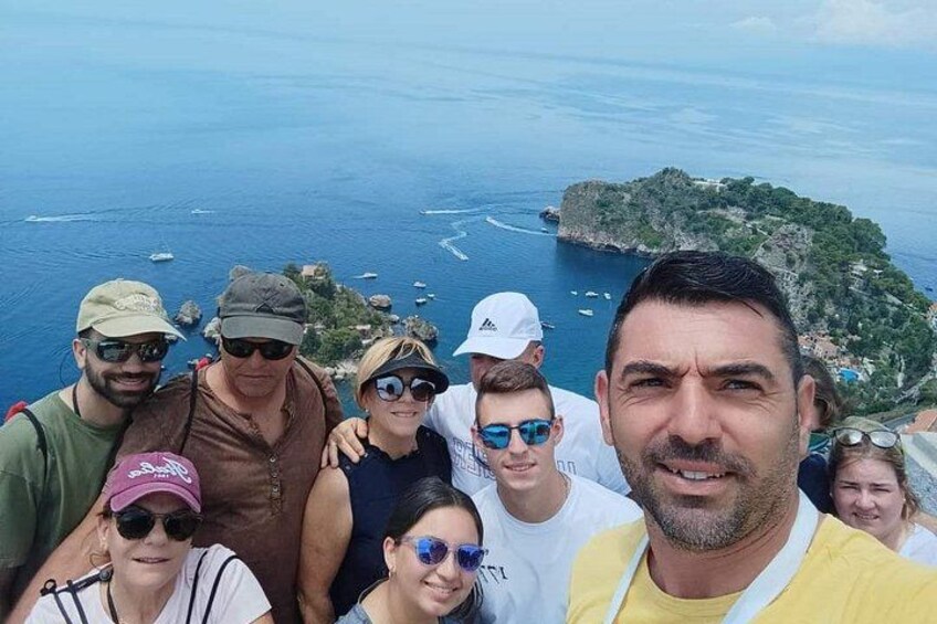 Un gruppo di persone su una scogliera con vista su una zona costiera, barche e una piccola isola. 3