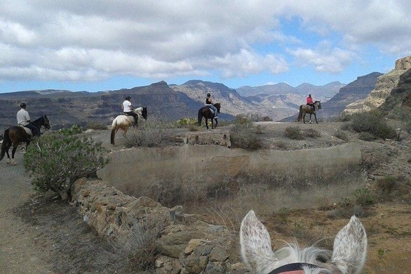 A group of people riding horses on a rocky terrain with mountains in the background. 2
