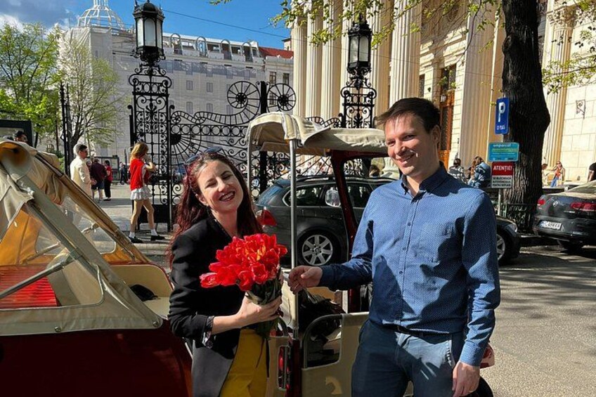A man and a woman standing next to a yellow taxi on a city street with buildings and a lamppost in the background. 4