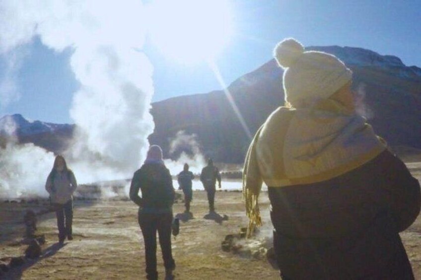 A group of people observing a geyser eruption in a dry, mountainous area. 5