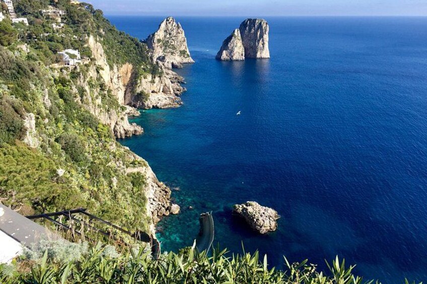 A coastal landscape with rocky cliffs, clear blue sea, and a prominent rock formation. 3