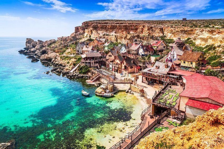 A coastal village with houses, a cliff, and clear turquoise waters. 2