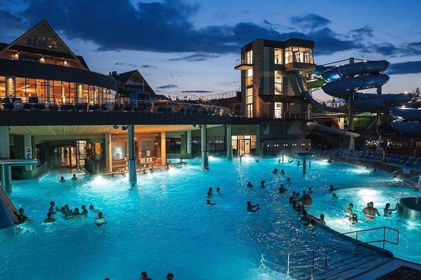 A swimming pool with people, a water slide, and a building with a unique architecture. 1