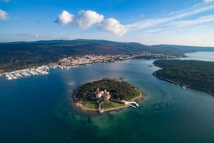 An aerial view of a coastal town with a central island, a bridge connecting the island to the mainland, and a large body of water surrounding the area. 4