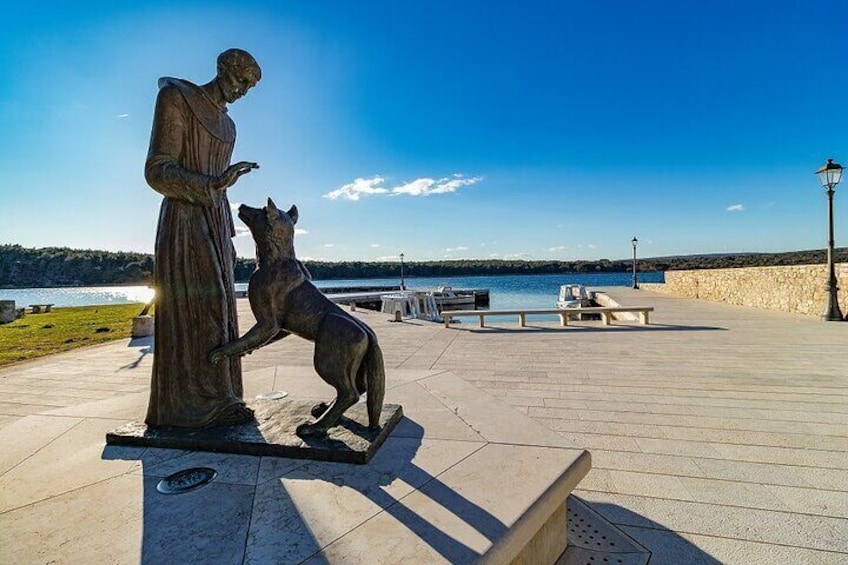A statue of a man and a dog on a platform by the water. 1