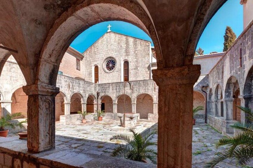 A courtyard with stone arches, a building with a cross, and potted plants. 2