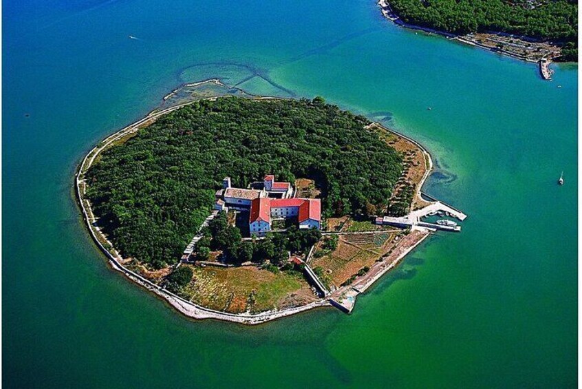 An aerial view of a small island with a red-roofed building surrounded by lush greenery and clear turquoise waters. 5