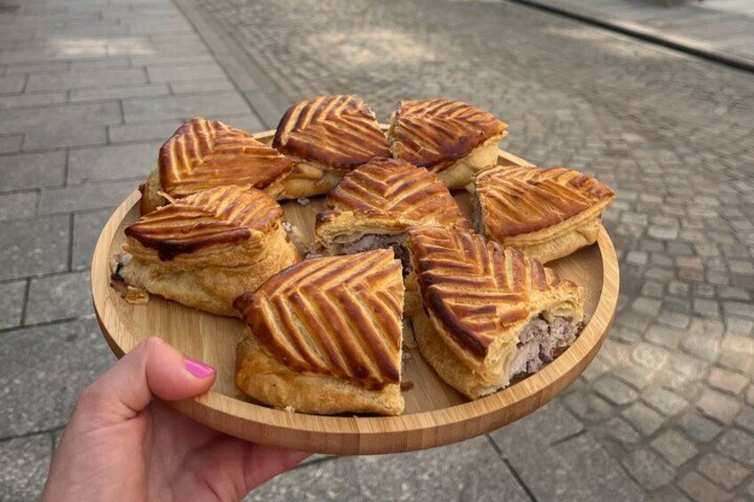 A hand holding a wooden plate with several triangular pastries. 2