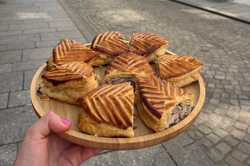 A wooden plate with several triangular pastries, held by a hand with pink nail polish. 4
