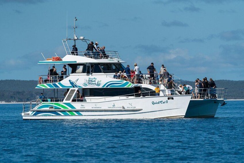 A white and blue boat named 'Quick Cat II' with people on deck and a forested coastline in the background. 3