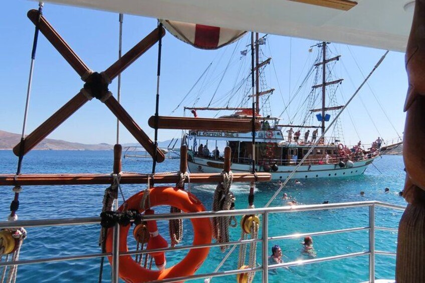 En båt med människor som simmar i vattnet, en livboj och en segelbåt i bakgrunden. 2