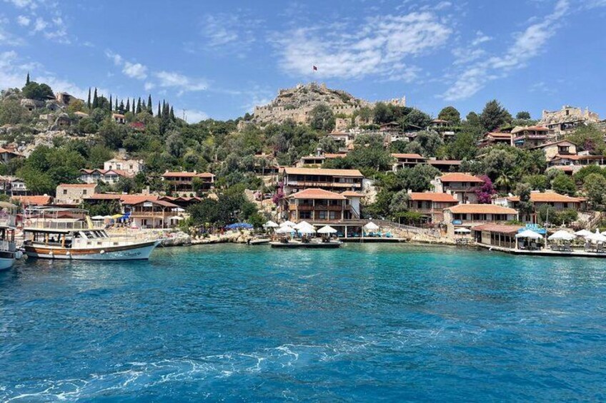 A coastal town with buildings, boats, and a hill with ruins. 2
