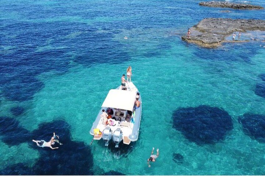 A boat with people swimming in clear blue water. 1
