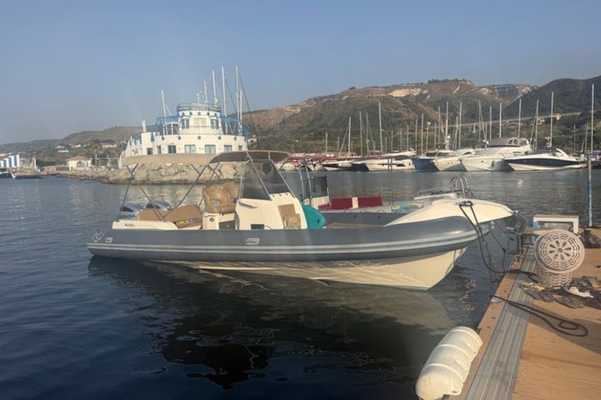 A boat docked at a marina with other boats in the background and a building on a hill. 4