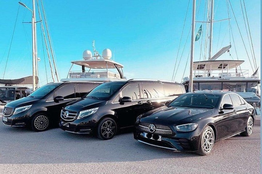 Trois voitures noires de marque Mercedes-Benz sont garées dans un port de plaisance, avec des voiliers en arrière-plan. 5