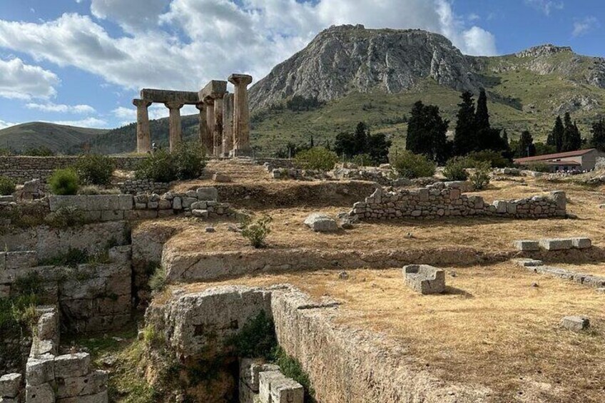 Ancient ruins with columns and stone structures, set against a mountainous backdrop. 1