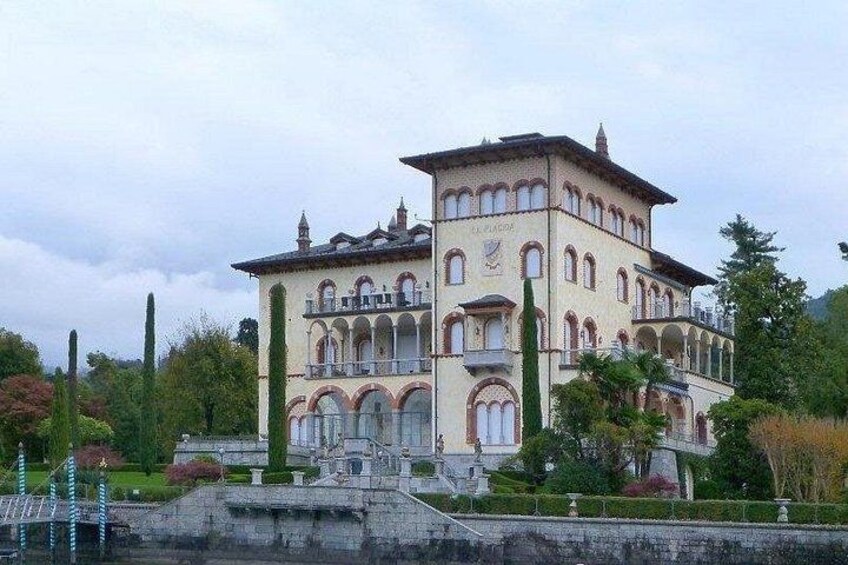 A large, multi-story building with arched windows and balconies, surrounded by lush greenery and a body of water. 3