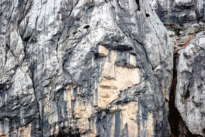 A rugged cliff face with visible stratification and a small stream running along the base. 5