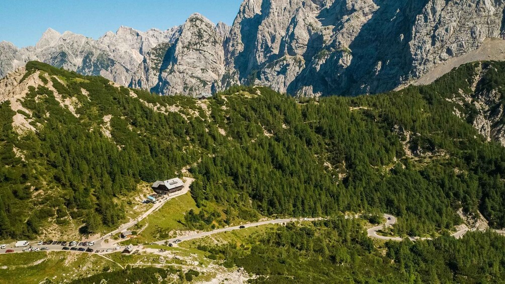 A mountainous landscape with a winding road, a building with a sloped roof, and dense forest. 3